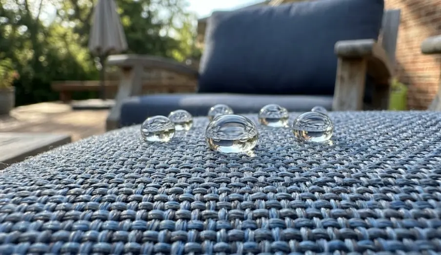 Water beading on outdoor cushion fabric after applying DWR fabric protector — bead test showing effective treatment